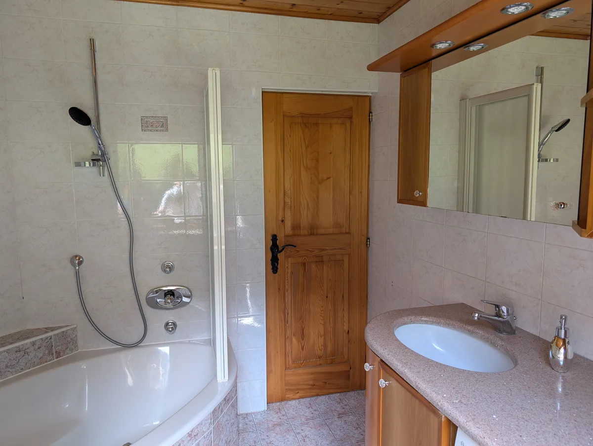 Bagno con vasca ad angolo, divisorio doccia in vetro e un lavabo sotto uno specchio illuminato