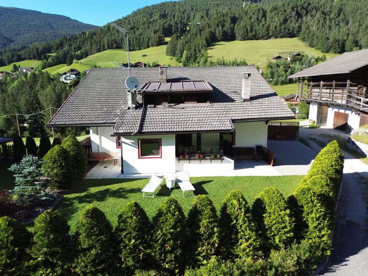 La casa vista dall'alto, lettini sul prato privato, con prati e pendii boscosi che si innalzano dietro
