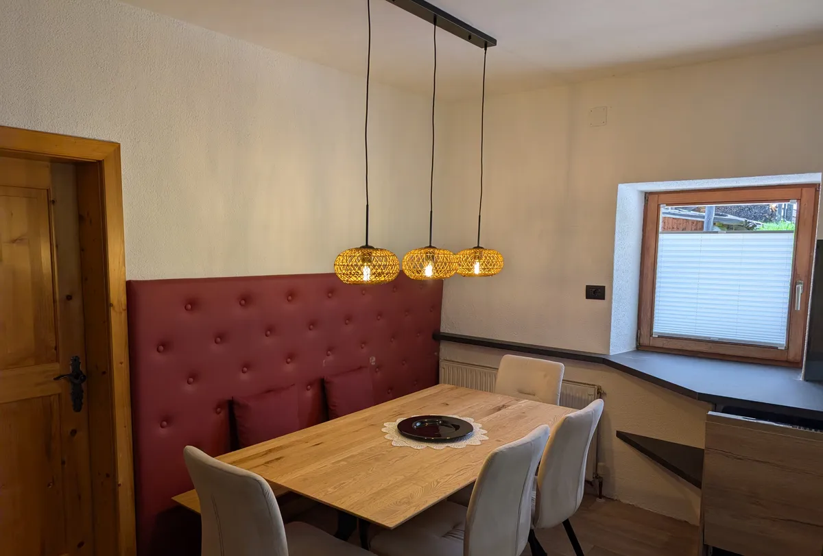 Tavolo da pranzo con lampade a sospensione intrecciate sopra una panca imbottita bordeaux, accanto a una finestra affacciata sul giardino