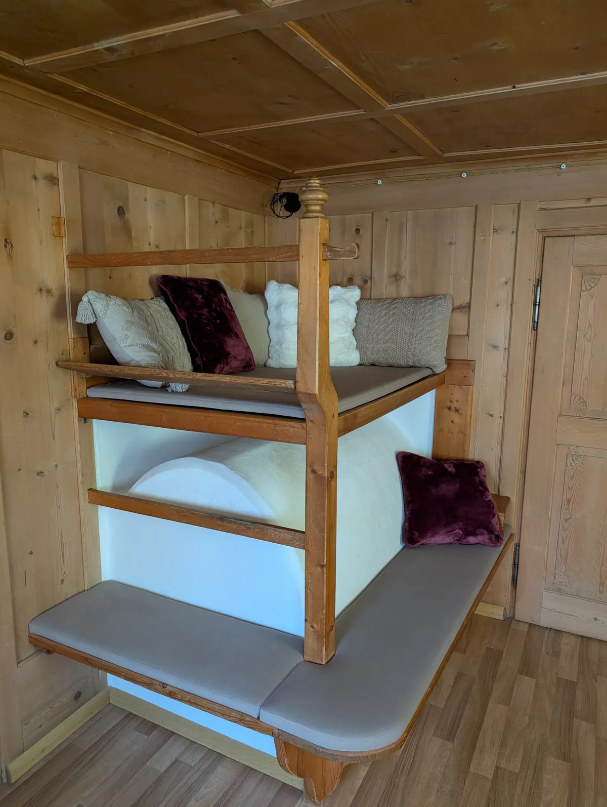 Letto a castello in legno incassato con cuscini panna e bordeaux sopra una panca imbottita, in una stanza rivestita di legno