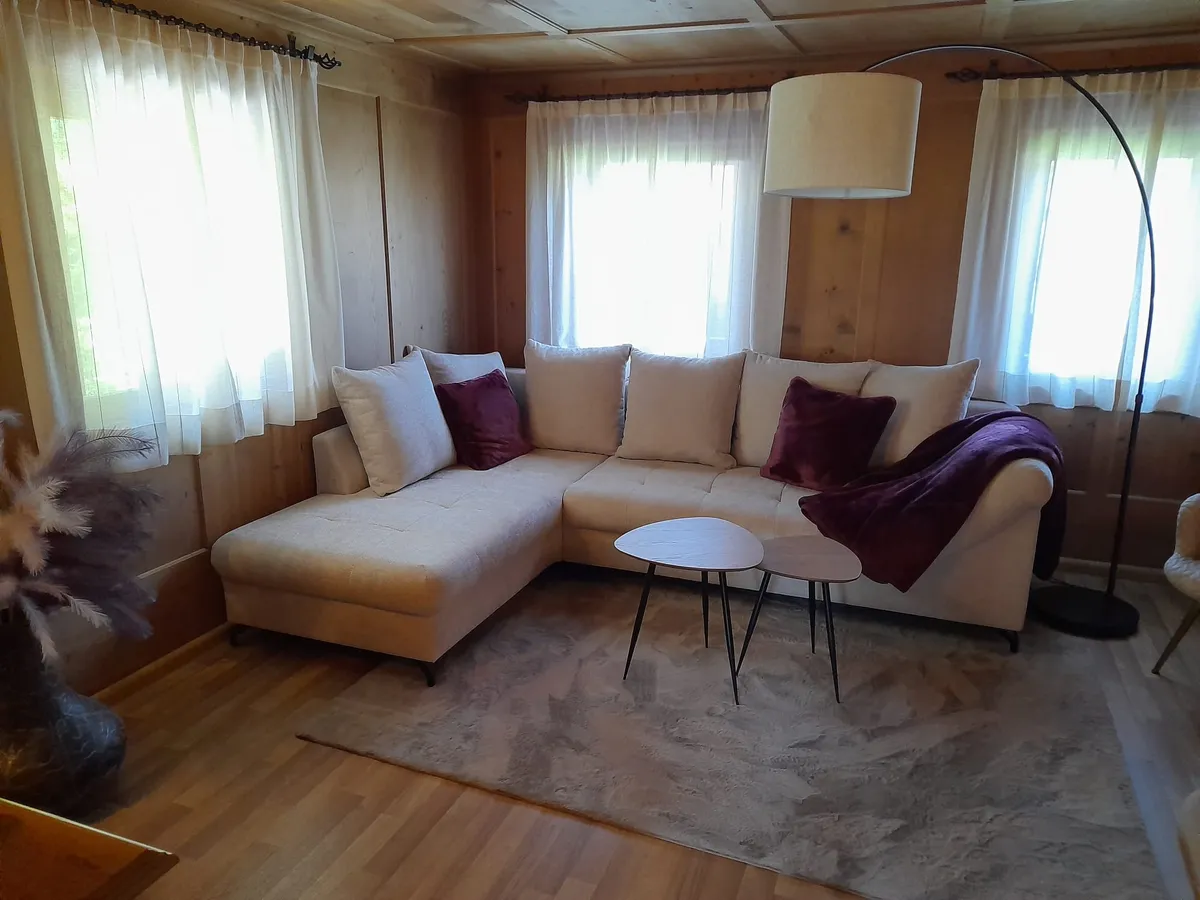 Soggiorno con divano angolare beige e due ampie finestre affacciate sul giardino